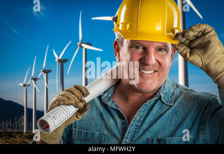 Smiling Contractor in Hard Hat Holding Extention Cord Outdoors Near Wind Turbines. Stock Photo