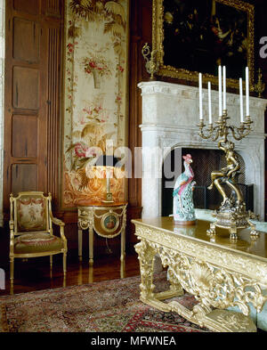 Traditional drawing room with wood panelling, marble fireplace, gilded furniture, and an oriental rug and tapestry. Stock Photo