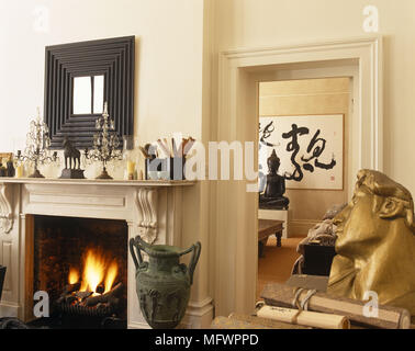 Mirror above fireplace with lit fire next to antique sculptures and artwork Stock Photo