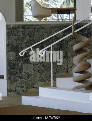 Modern sculpture next to white staircase in front of exposed stone wall Stock Photo