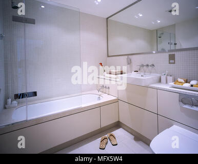 Modern bathroom with mosaic tiled walls, bathtub with glass partition, mirror, and a washbasin on a countertop. Stock Photo