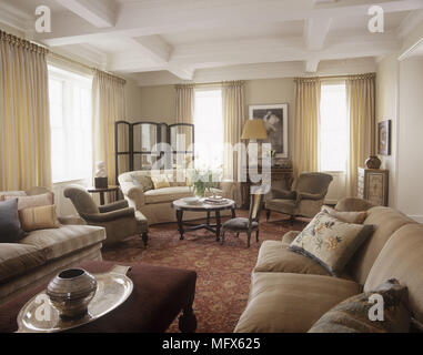 A traditional sitting room with sofas and chairs beamed ceiling windows curtains red floral pattern carpet Stock Photo