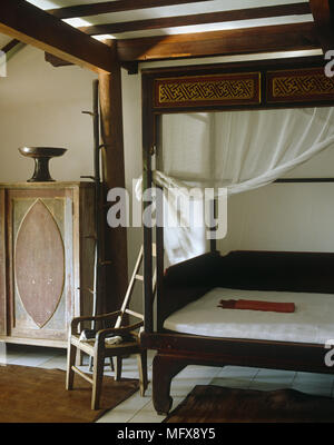 Wooden chair next to period style four poster bed with curtains Stock Photo