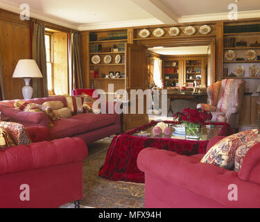 Upholstered red sofa and armchairs around coffee table in sitting room Stock Photo