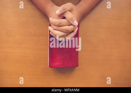 Top view of man praying on holy bible in the morning.teenager boy hand with Bible praying,Hands folded in prayer on a Holy Bible in church concept for Stock Photo