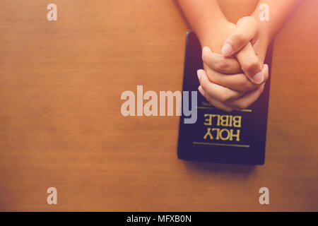 Top view of man praying on holy bible in the morning.teenager boy hand with Bible praying,Hands folded in prayer on a Holy Bible in church concept for Stock Photo