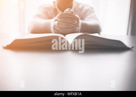 man praying on holy bible in the morning.teenager boy hand with Bible praying,Hands folded in prayer on a Holy Bible in church concept for faith, spir Stock Photo