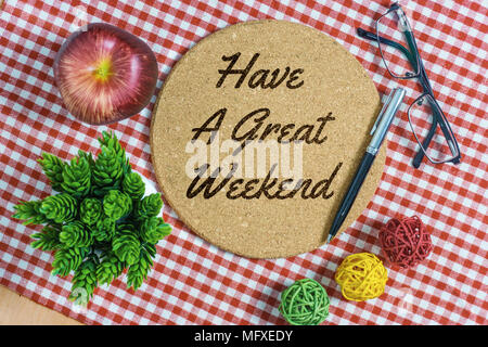 Have A Great Weekend. Cork bulletin board on red stripes napkin with pen, apple, spectacle and potted plant. Stock Photo