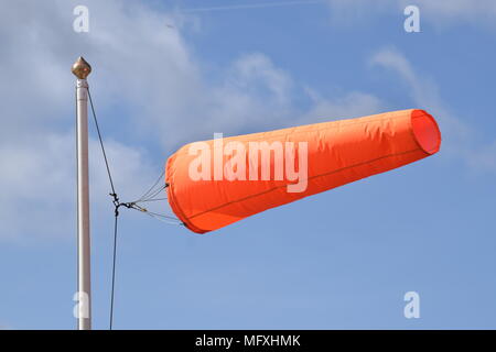 ORANGE WINDSOCK FLYING HORIZONTALLY IN A SOUTHERLY WIND, AGAINST A BACKGROUND OF WHITE CLOUDS IN A BLUE SKY. Stock Photo