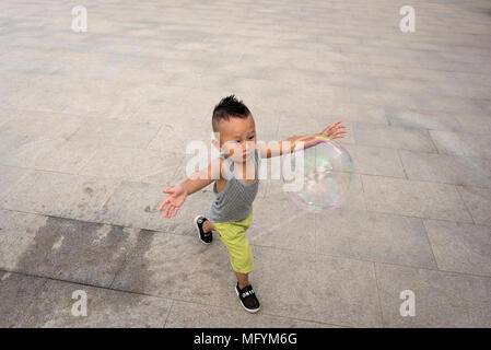 Grandfather creates giant bubbles for grandson while playing in city square, Xilinhot, Inner Mongolia, China Stock Photo