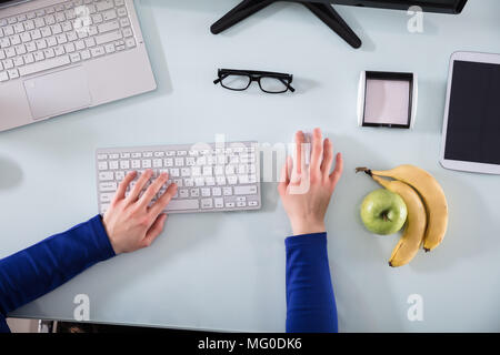 Elevated View Of Businessperson's Hand Working On Computer Keyboard With Fresh Fruits On Desk Stock Photo