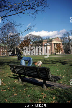 A student at Dartmouth College lays on a park bench located on 'The Green' reading a book at Hanover, New Hampshire, United States, North America. Stock Photo