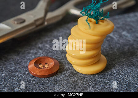 Sewing buttons, thread, scissors on needle punched nonwoven fabric background. Macro view, shallow depth of field. Stock Photo