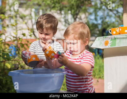 Two small boys washing dishes outdoors in village, in country Stock Photo