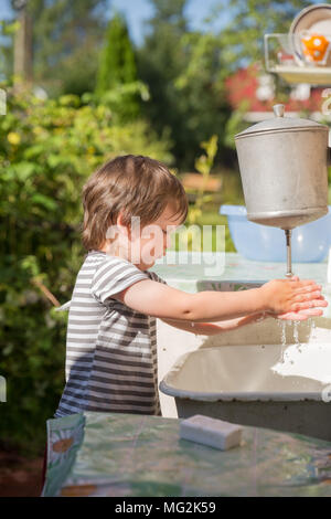 Little boy, 4 years old, in striped T-shirt washes his hands under washstand outdoors in countryside Stock Photo