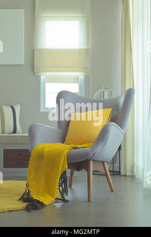 Easy armchair in gray color with scarft, pillow and area rug in yellow color scheme Stock Photo