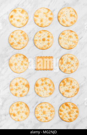 Rows of round crackers and a square tea biscuit in the middle, on marble background. Stock Photo