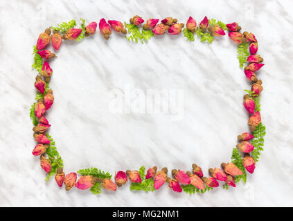 Frame made of dried roses and green leaves, on marble background. Stock Photo