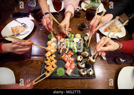 A set of sushi rolls on a table in a restaurant. A party of friends eating sushi rolls using bamboo sticks. Stock Photo