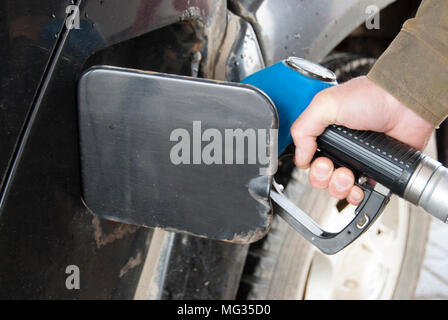 A man's hand holds a refueling gun at a gas station and runs an old dirty car. Stock Photo