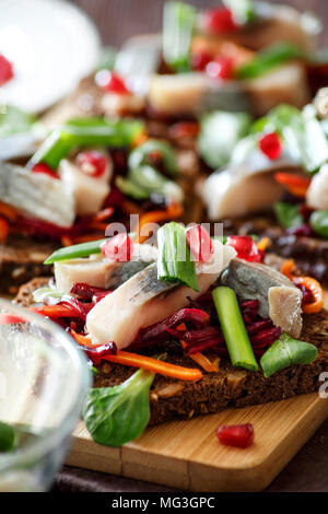 Bruschetta on rye bread with fried straws of beet and carrots, greens and slices of herring on a bamboo board.  Selective focus. Stock Photo
