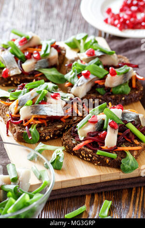 Bruschetta on rye bread with fried straws of beet and carrots, greens and slices of herring on a bamboo board.  Selective focus. Stock Photo