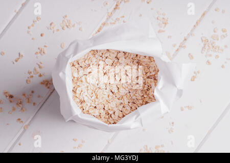 overhead view of bag of rolled oats oatmeal oat flakes on rustic white wooden table Stock Photo