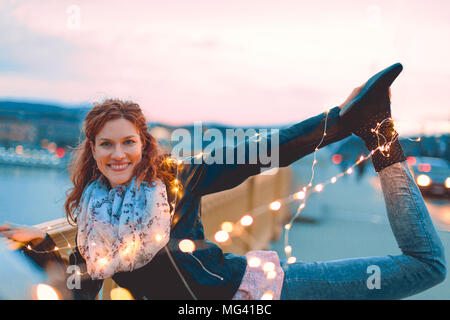 Young redhead woman posing with fairy lights outdoors and smile, teal and orange style Stock Photo