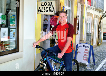 Young blond man with portuguese national  soccer team shirt sitting on a bike and smiling to the camera Stock Photo