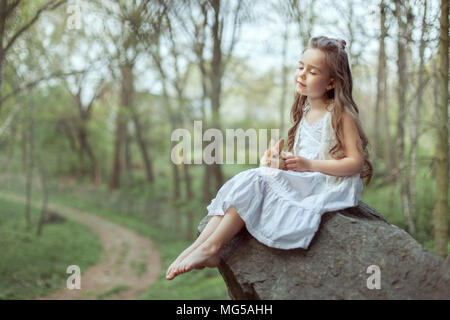 Little girl sits on a cliff. She closed her eyes and held a small rabbit in her hands. Stock Photo