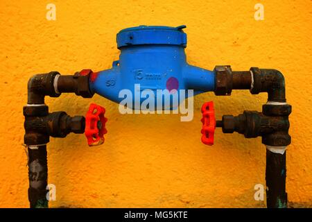 Old Blue Water Meter With Yellow Painted Concrete Wall Background. Stock Photo