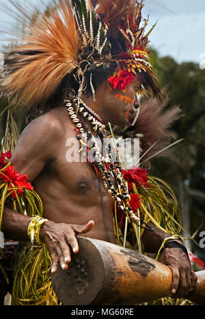 Papua New Guinea - November 8, 2010:  A man with tribal face painting and wearing special clothing is playing a Kundu Drum on a festival. Stock Photo