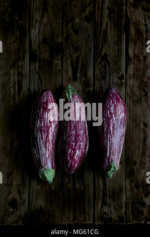 Three Nubia eggplants over a rustic wooden table in a darkness ambient. Stock Photo
