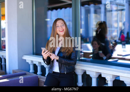 Jocund woman typing by smartphone at street cafe. Concept of enjoying social networks. Stock Photo