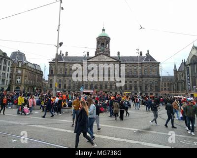 Amsterdam, The Netherlands - April 27th, 2018 : King's Day - group of people in front of the famous square; King's Day (formerly Queen's Day) festivities invite locals and visitors alike to soak up Amsterdam's open-air fun. In the streets, canals, parks and everywhere in between, the city is bursting with orange as Amsterdammers enjoy the biggest street party of the year.;  Credit: Bala Divakaruni/Alamy Live News Stock Photo