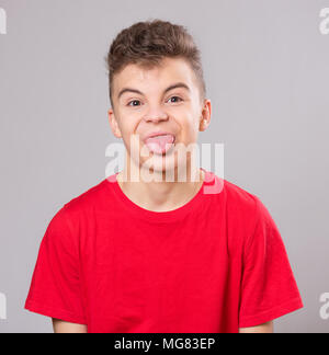 Emotional portrait of cut teen boy showing his tongue. Funny teenager puts out tongue, on gray background. Stock Photo