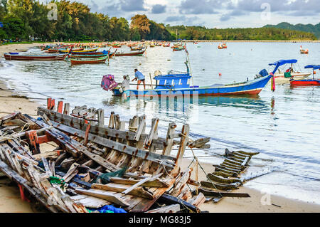 Phuket, Thailand - November 19, 2012: Boat wreck on beach & traditional long-tail & speed boats used for fishing & tourist trips moored in bay. Stock Photo
