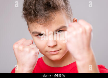 Emotional portrait of irritated teen boy. Furious teenager looking with anger at camera. Handsome outraged child threatens with a fist, isolated on wh Stock Photo