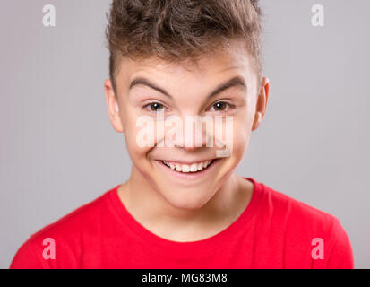 Silly teen boy making grimace - funny face. Child on gray background. Emotional portrait of caucasian teenager looking at camera. Stock Photo