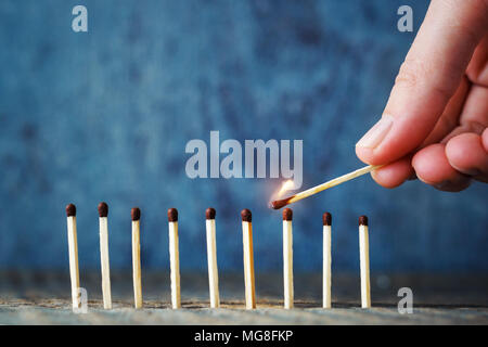 A lit match in hand tries to set another match on fire. The concept of unity and mutual assistance. Burning match on a wooden blue background Stock Photo