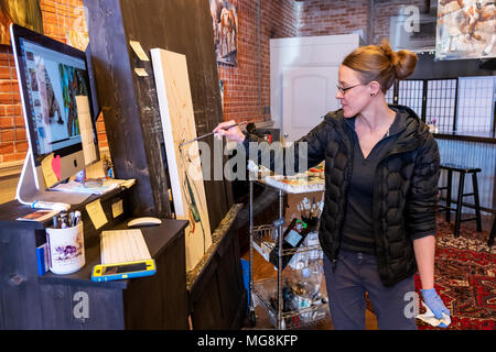 Fine artist Katie Maher referencing a computer image while creating an oil painting in her gallery; Salida; Colorado; USA Stock Photo