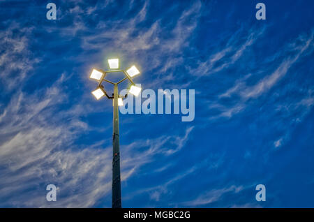 Six streetlights in a hexagonal pattern under a blue sky with dramatic clouds. Powered on for the evening. Stock Photo