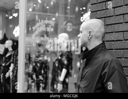 Man with shaved head looking into shop window at mannequins, black and white Stock Photo