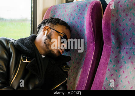 Young man wearing sunglasses, sitting on train, sleeping Stock Photo