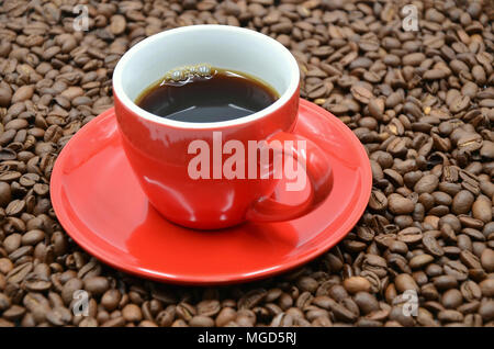Red cup with saucer filled with coffee on coffee beans Stock Photo