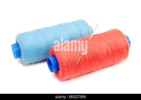 Spools of sewing thread of blue and red, with them stuck in a sewing needle isolated on white background. Stock Photo