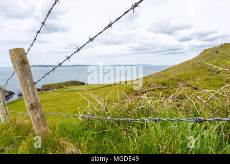 Antrim/N. Ireland - May 30, 2015: The rolling hillside of Antrim with a post and barbed wire fence.  Rathlin Island sits off in the distance. Stock Photo