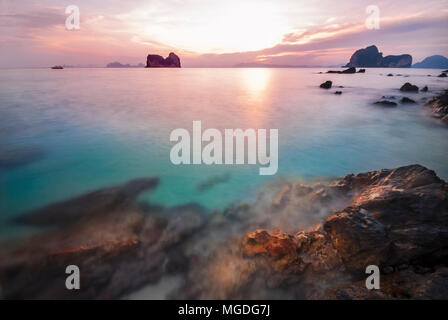 Sun rise on the rock beach on Ngai island in southern sea of Thailand. Mountain background against the colorful red sky and emerald turquoise blue wat Stock Photo