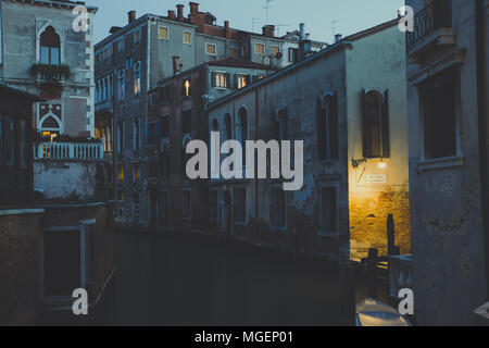 View of a Venice canal at dusk, while the faint light coming from the street lamps starts to illuminate the water creating a sort of magical effect Stock Photo