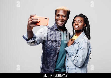 Portrait of a happy young african couple grimacing while standing together and taking a selfie isolated over gray Stock Photo